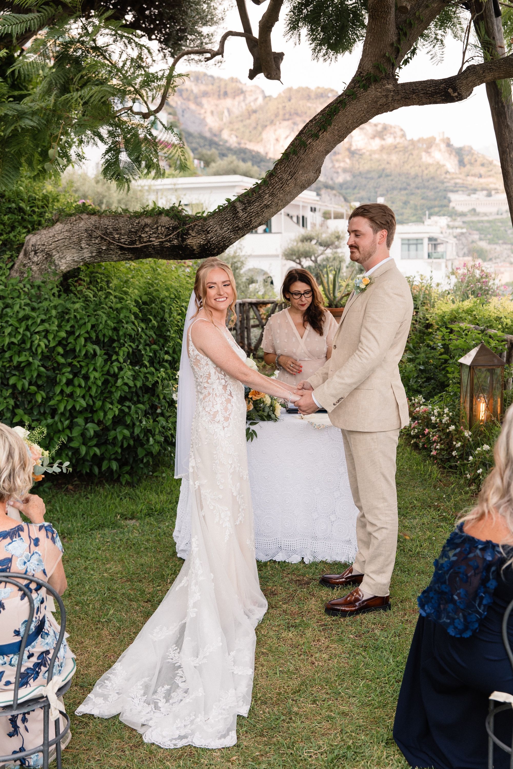Bride and groom holding hands in front of their guests and their celebrant with the Amalfi Ciast in the background