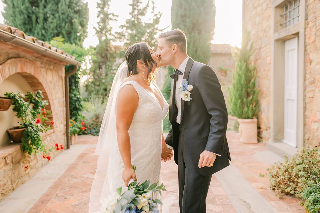 Newlyweds kissing with sunset hues and lush greenery in the background in Italy