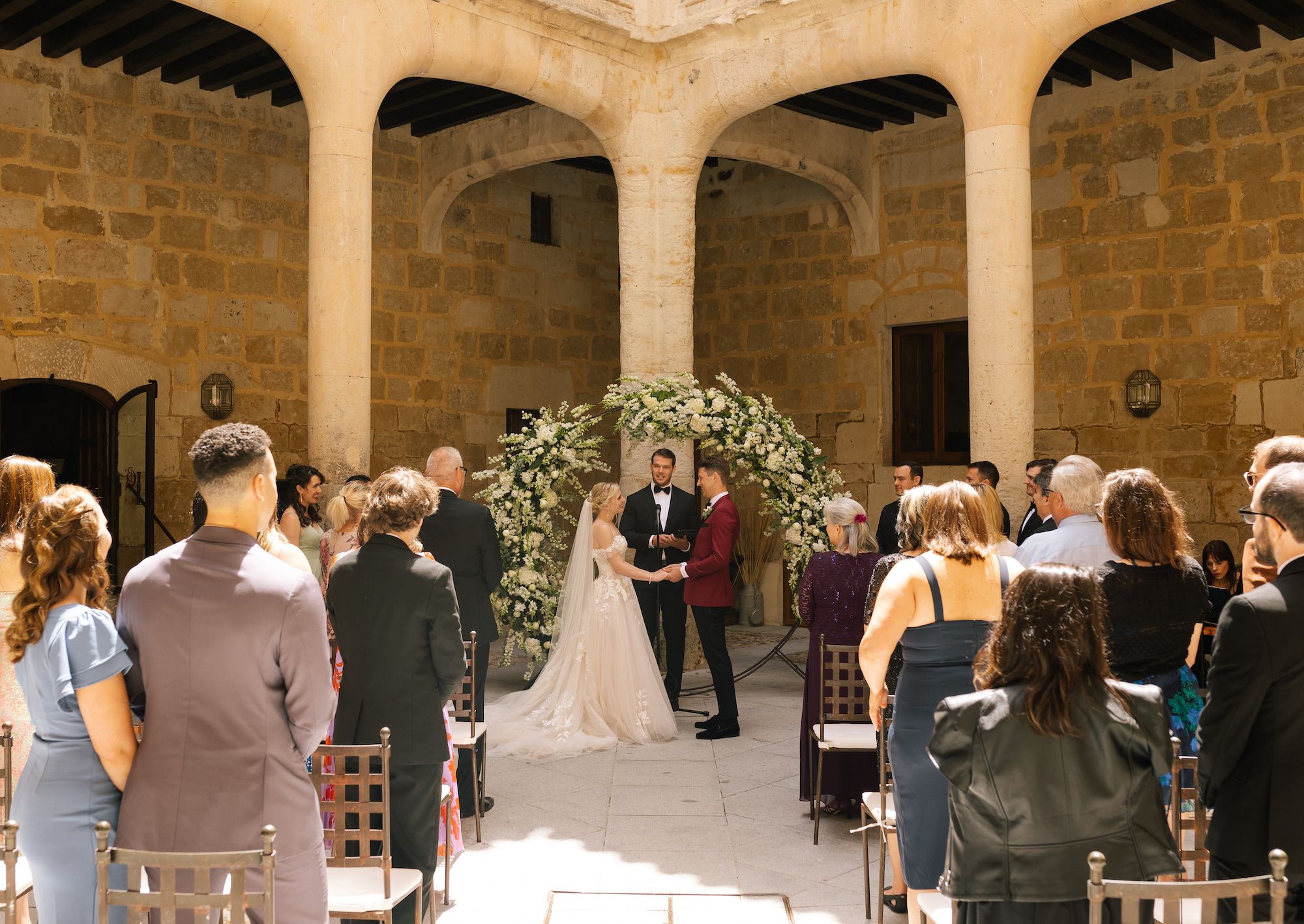 Bride and groom hold hands in front of guests in a wedding ceremony in a castle's courtyard in Spain