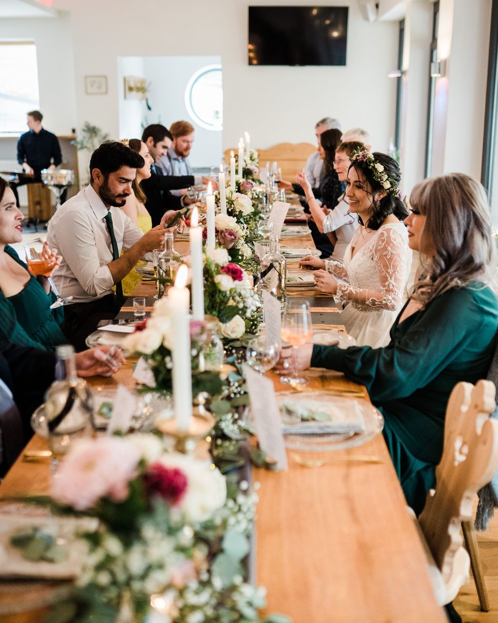A wedding party seated on wooden chairs and tables, having dinner during a wedding reception