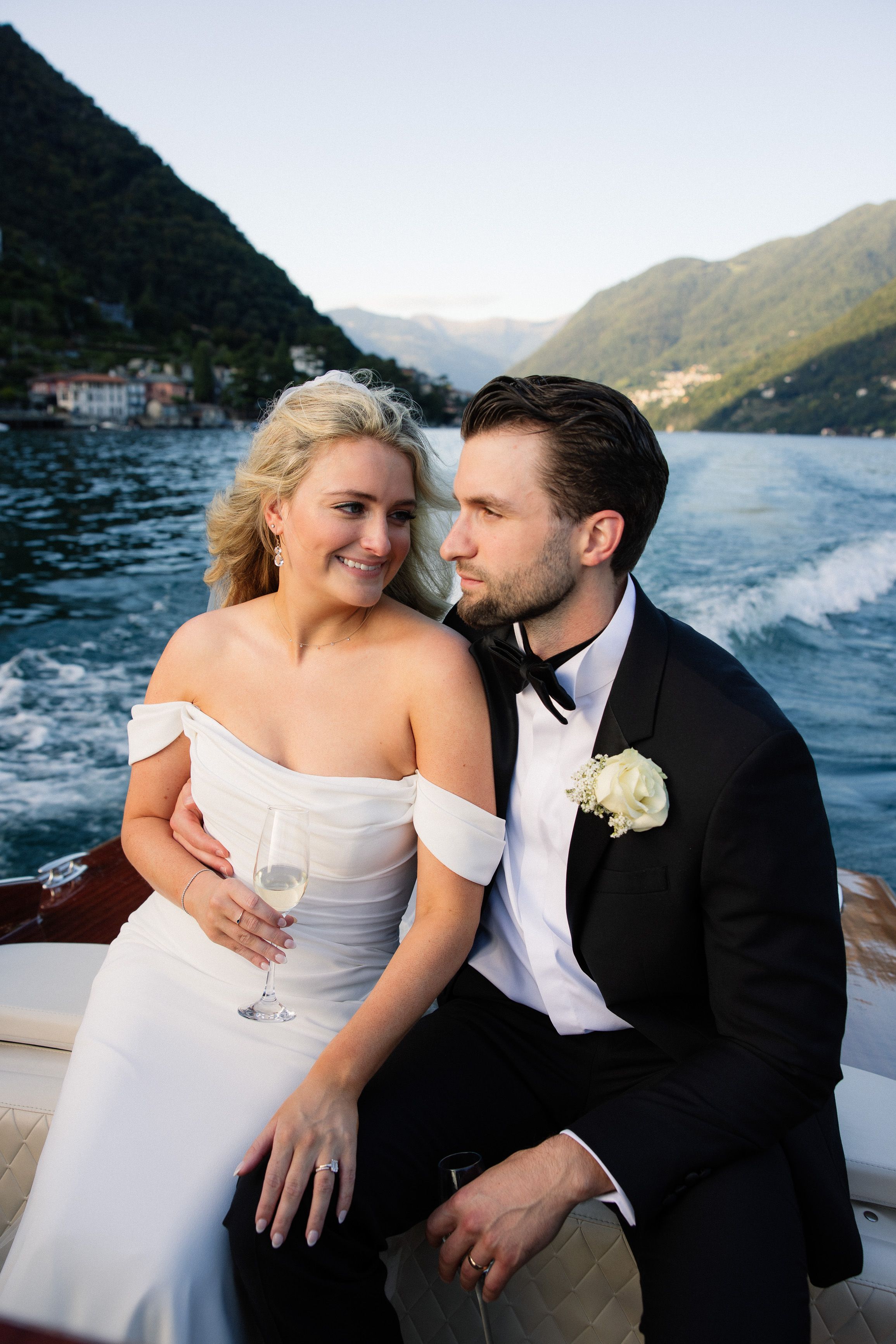 A bride and groom travel by boat for their intimate wedding in Italy set beside a beautiful lake and mountains