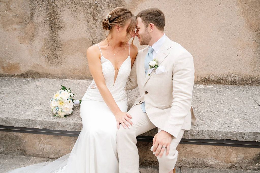 Bride and groom romantically looking at each other while sitting down in one of the areas of the castle where they got married in Italy