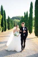 Bride and groom walking along an alley with cypress trees on both sides after the ceremony of their intimate wedding in Tuscany