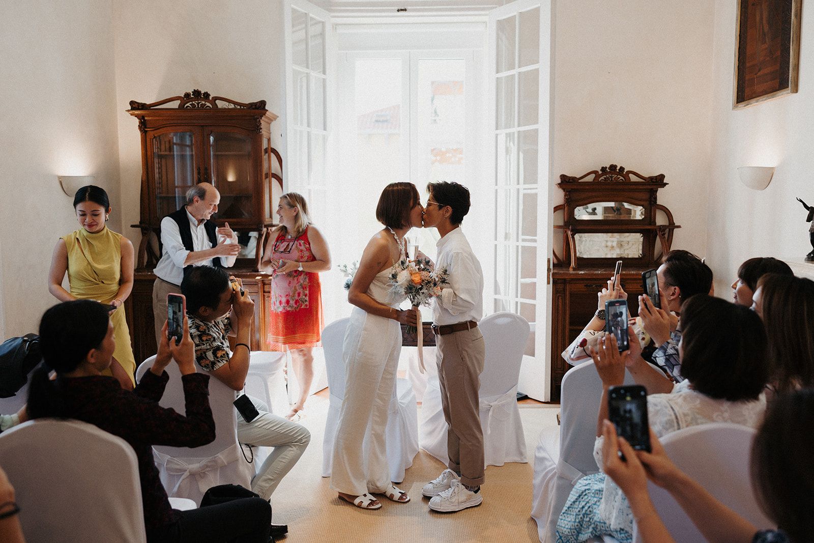 Two brides kiss inside a hotel's event room in Lisbon during their intimate wedding in Portugal