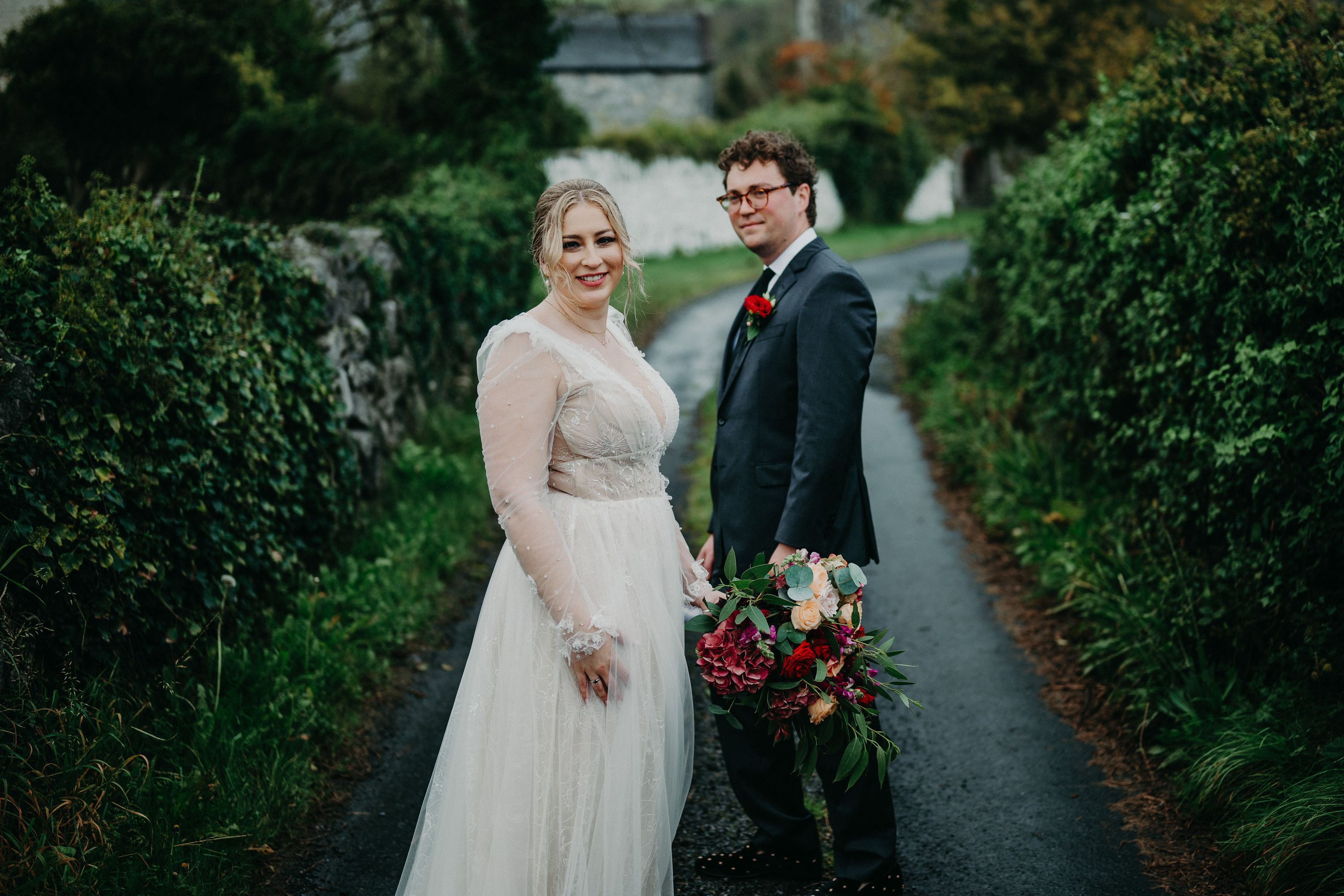 Newlyweds stand on a scenic country lane surrounded by lush hedges during an intimate wedding in Ireland