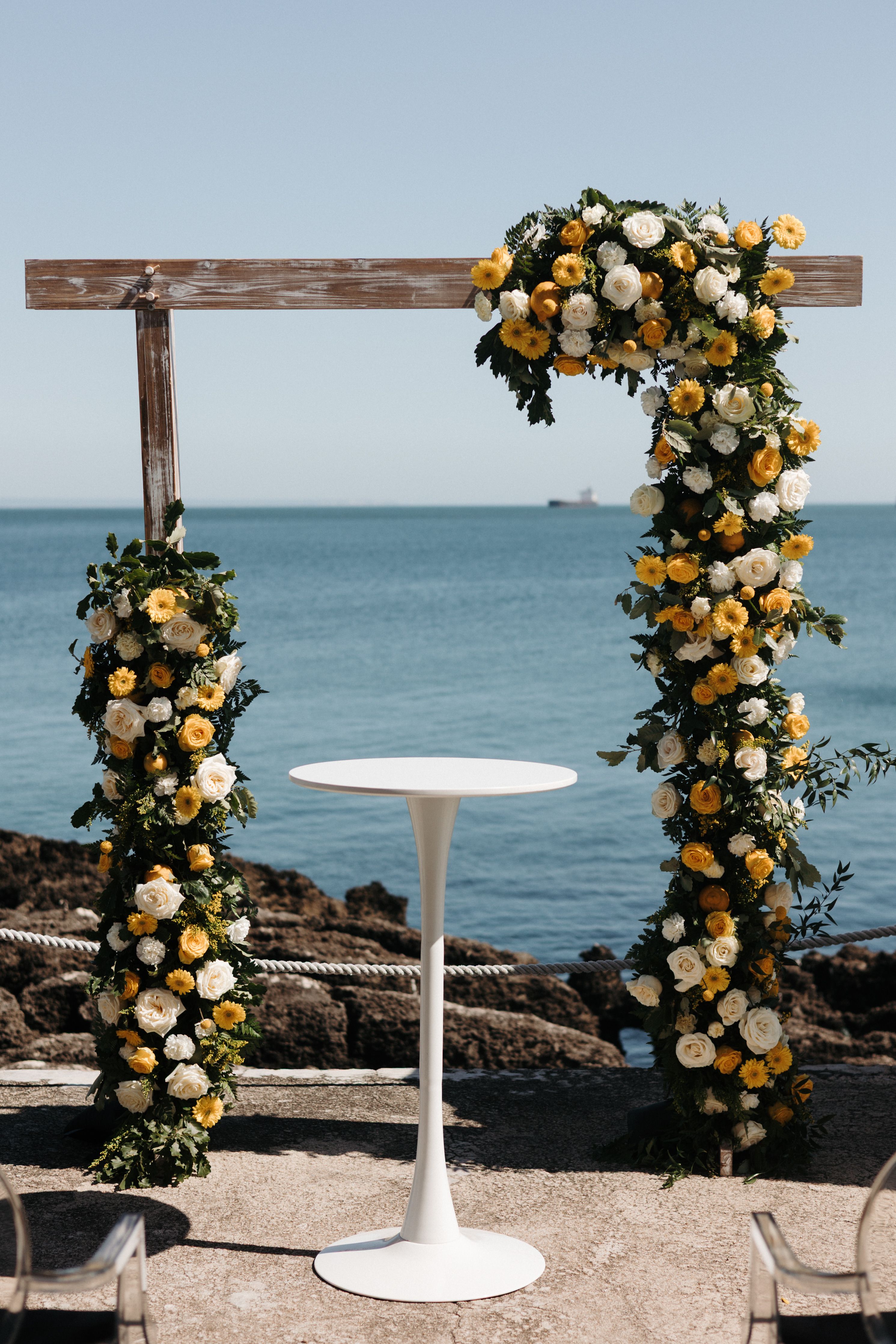 Wooden ceremony arch embedded with flowers and greens at the shore of a beach along the Cascais coast in Portugal