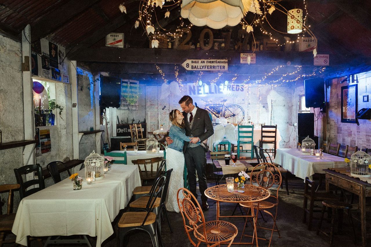 Newlyweds hugging each other inside a traditional Irish pub, with chairs and tables next to them and a stage at the back