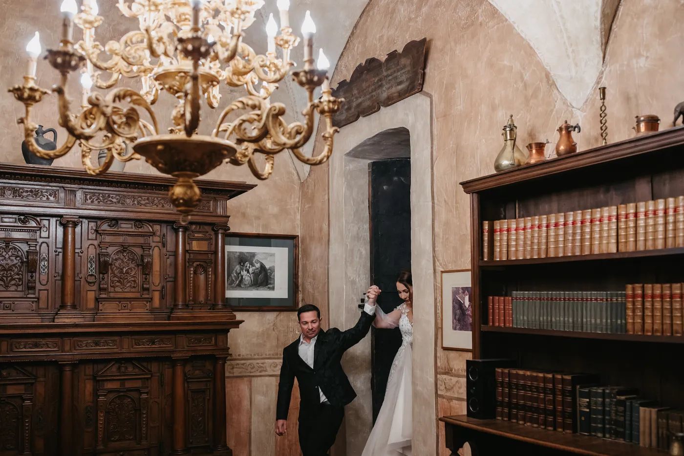 Groom leading his bride through a candlelit castle library in Tyrol