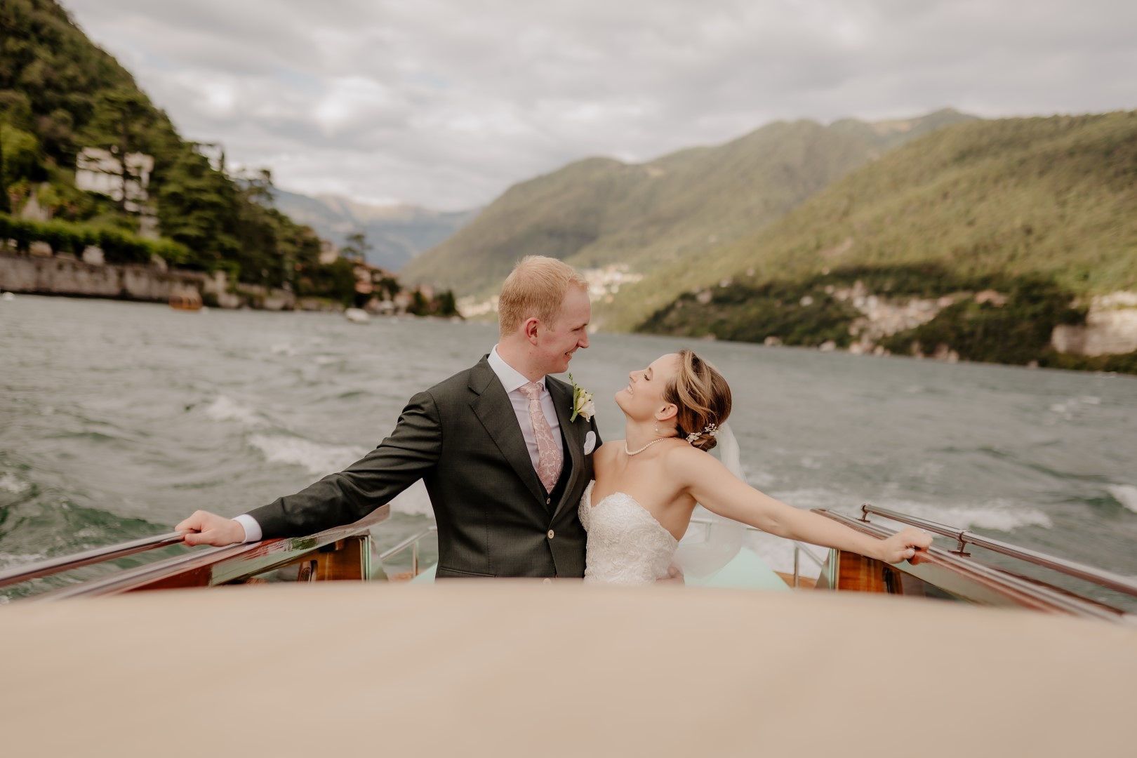 Newlyweds smiling and looking at each other as they ride a sailboat cruising the Lake Como for an elopement in Italy