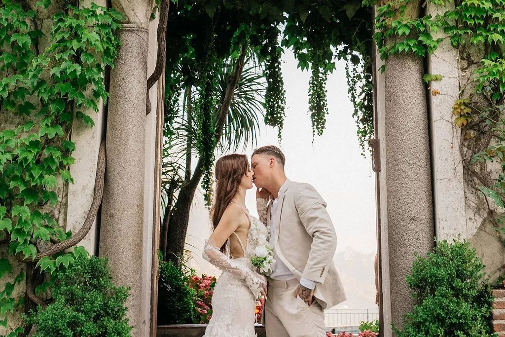 Newlyweds kissing each other with tall trees in the background during their small wedding in Italy