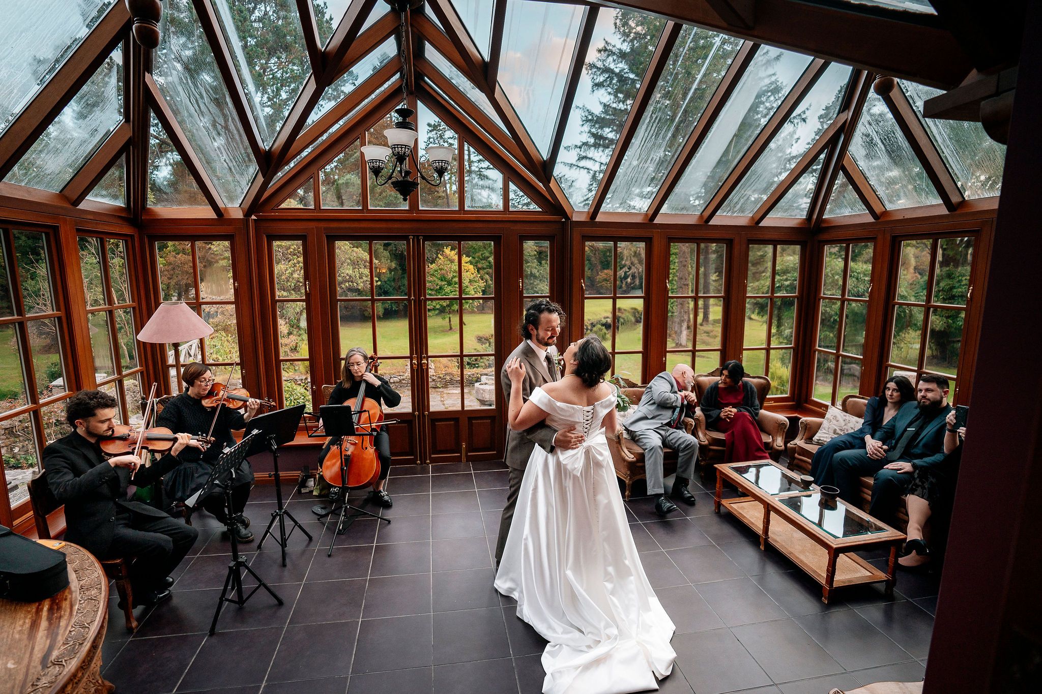 Bride and groom dance inside a glass-walled venue with guests around them during their elopement in Ireland