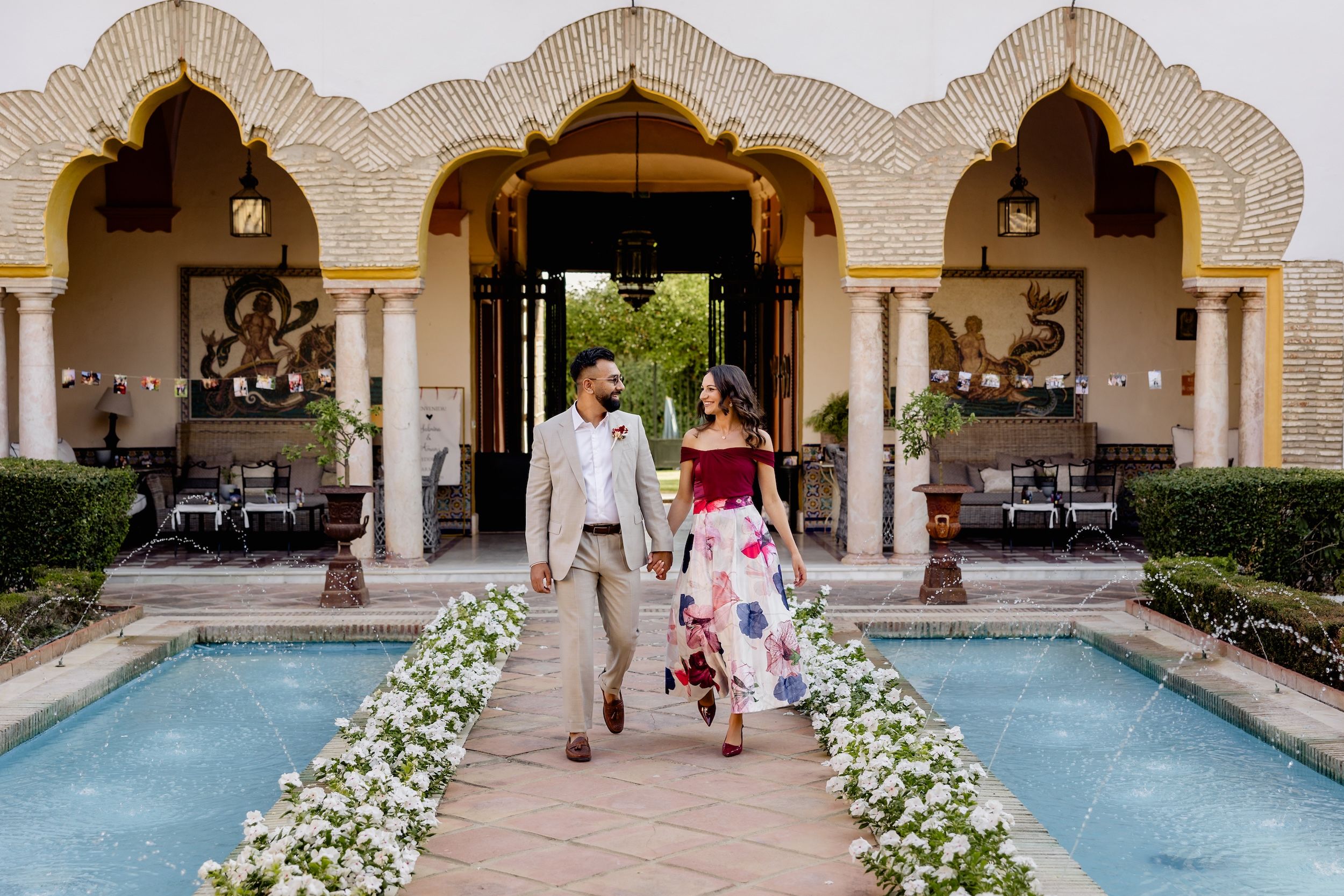 Bride and groom in casual attires walking in the middle of a pathway of the farmhouse where they got married in Spain