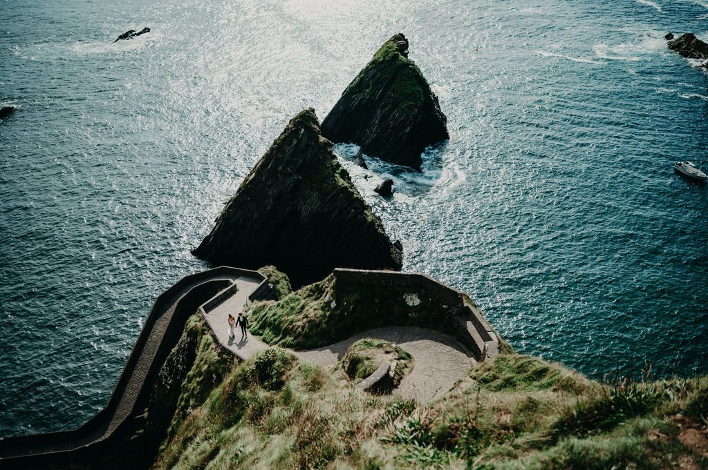 Wide shot of the Dunquin Pier with the Atlantic Ocean in the background and the couple barely seen walking on the zigzag path