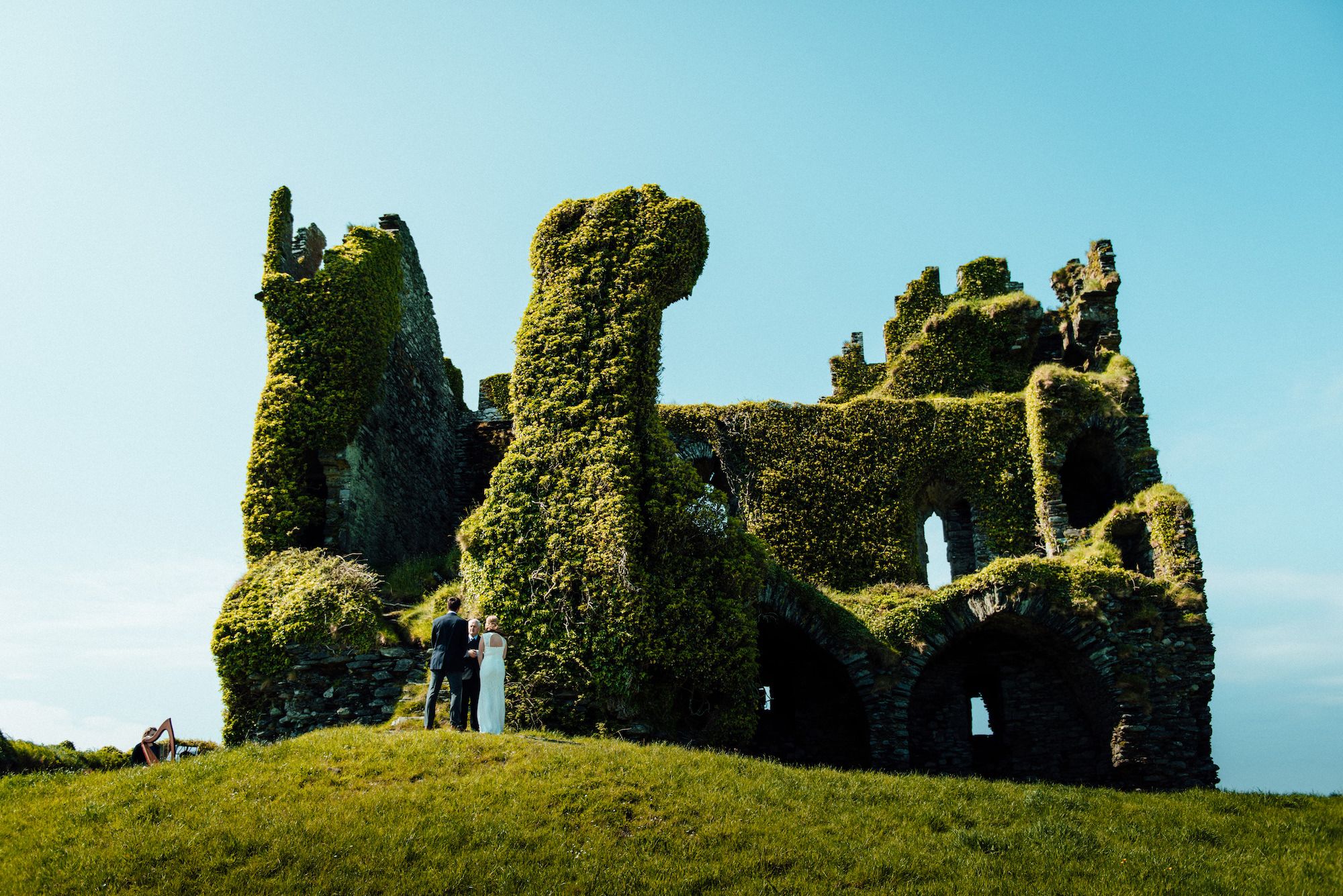 Couple having an elopement ceremony amidst the meadows of the Irish hills, in front of a castle ruin with crawling greenery