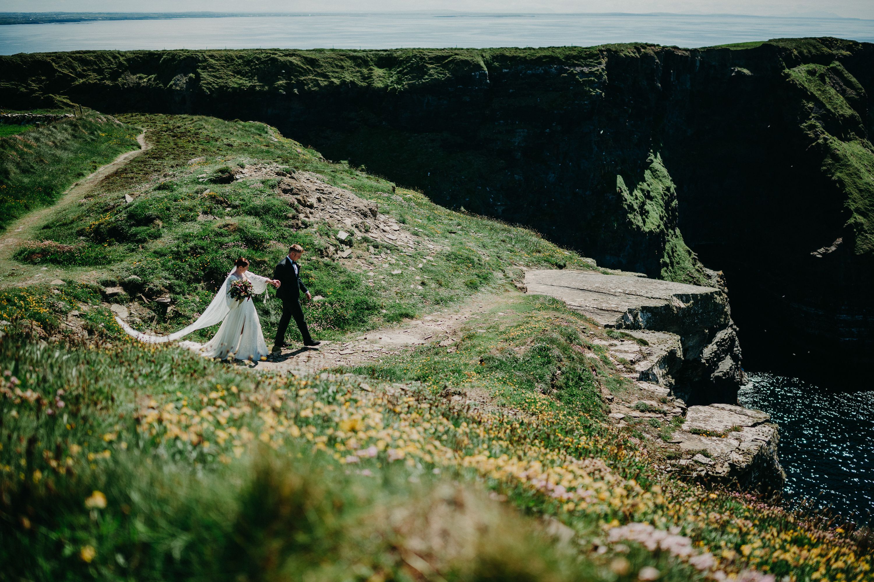 A bride and groom walking along a beautiful cliff after their small wedding in Ireland