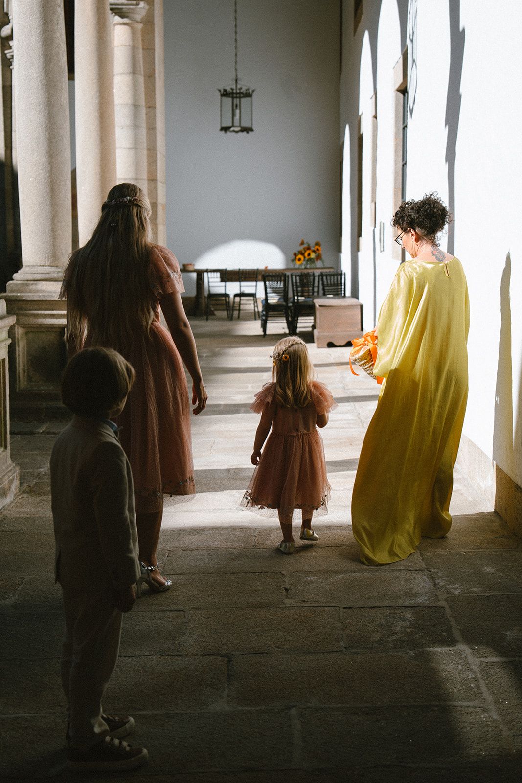 A flower girl and a small boy follow a bridesmaid along the cloister gallery toward the ceremony table at the Parador de Santiago.