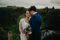 Bride and groom being romantic during the photoshoot of their destination wedding in Ireland, with the cliffs and a castle ruin in the background.