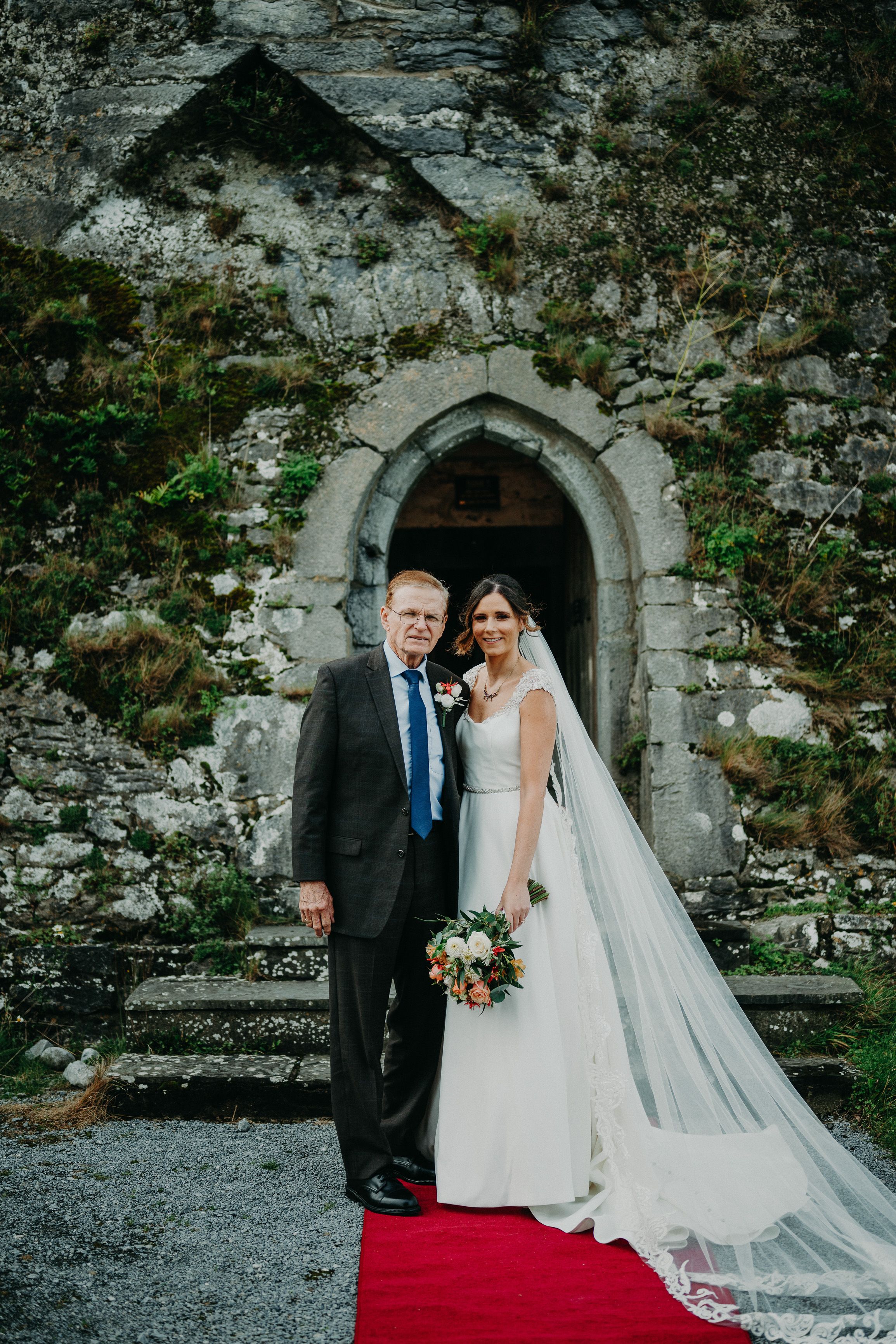 Bride and her father portrait beneath a historic stone archway during an intimate wedding in Ireland.