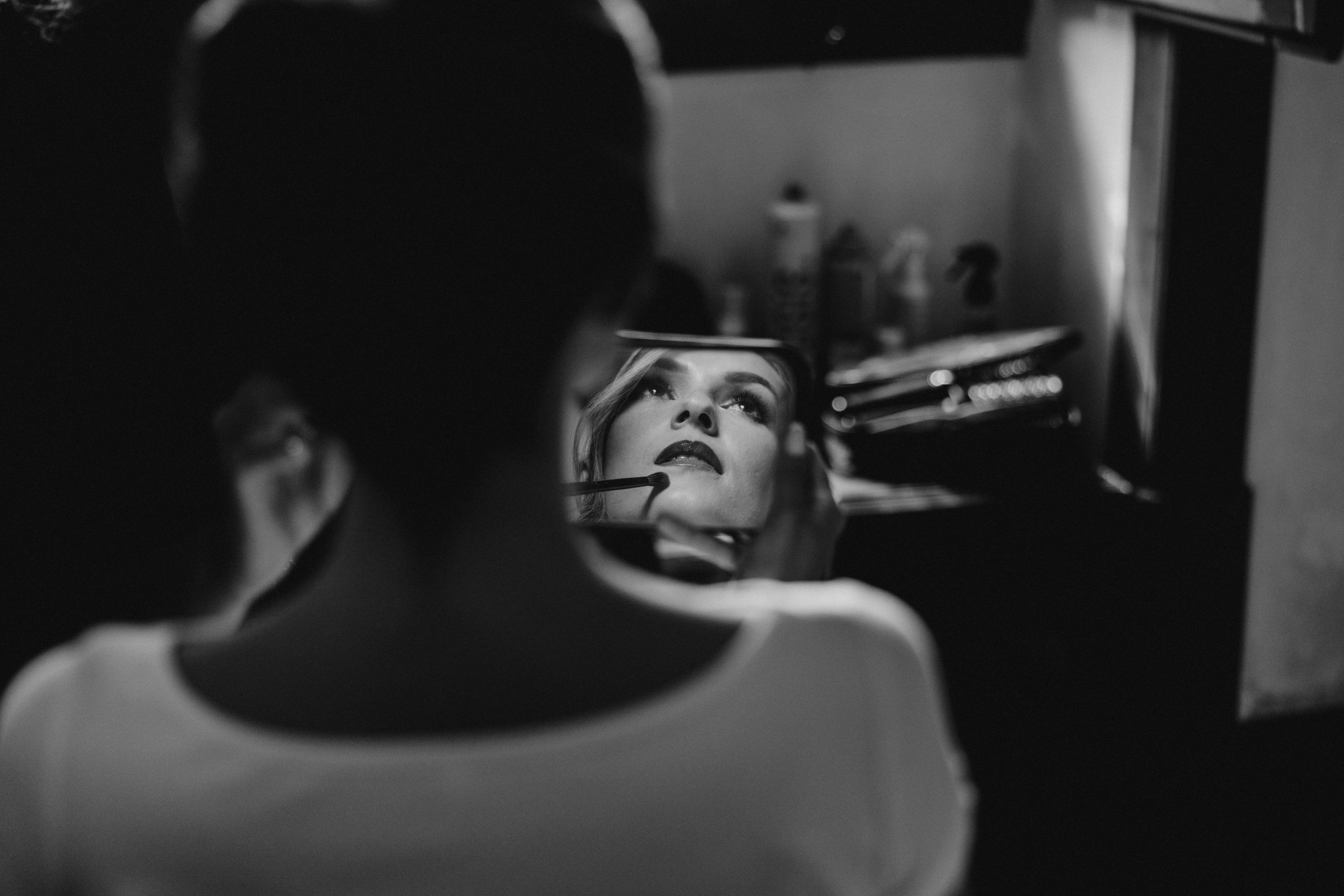 Black and white closeup photo of a bride touching up her makeup in the mirror