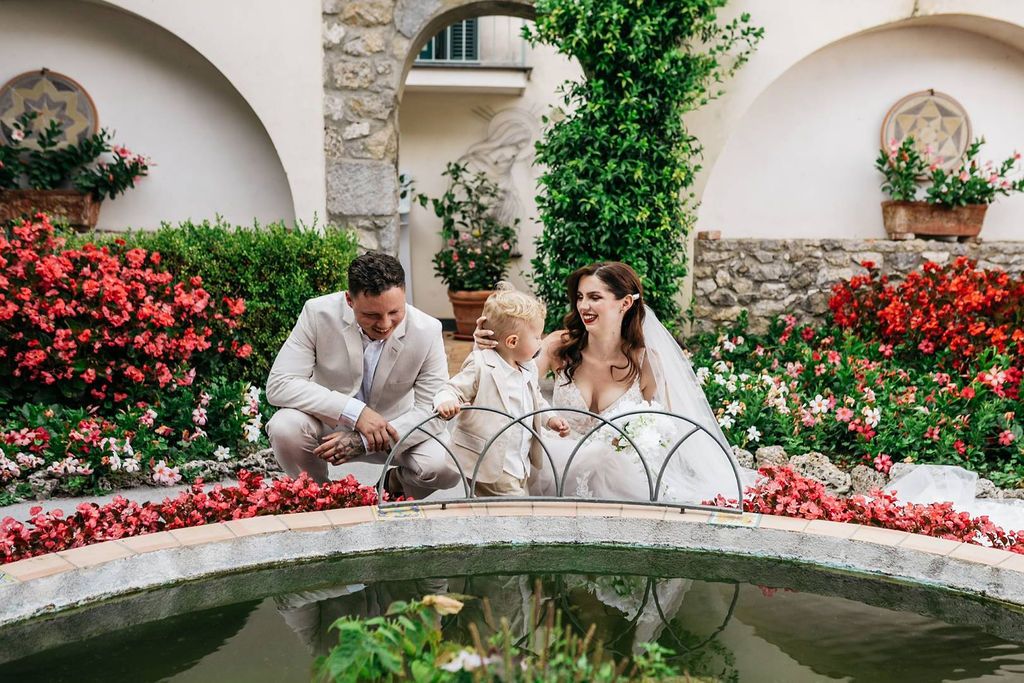 Bride and groom with their little son near the fountain of the garden of the hotel where they got married in Italy