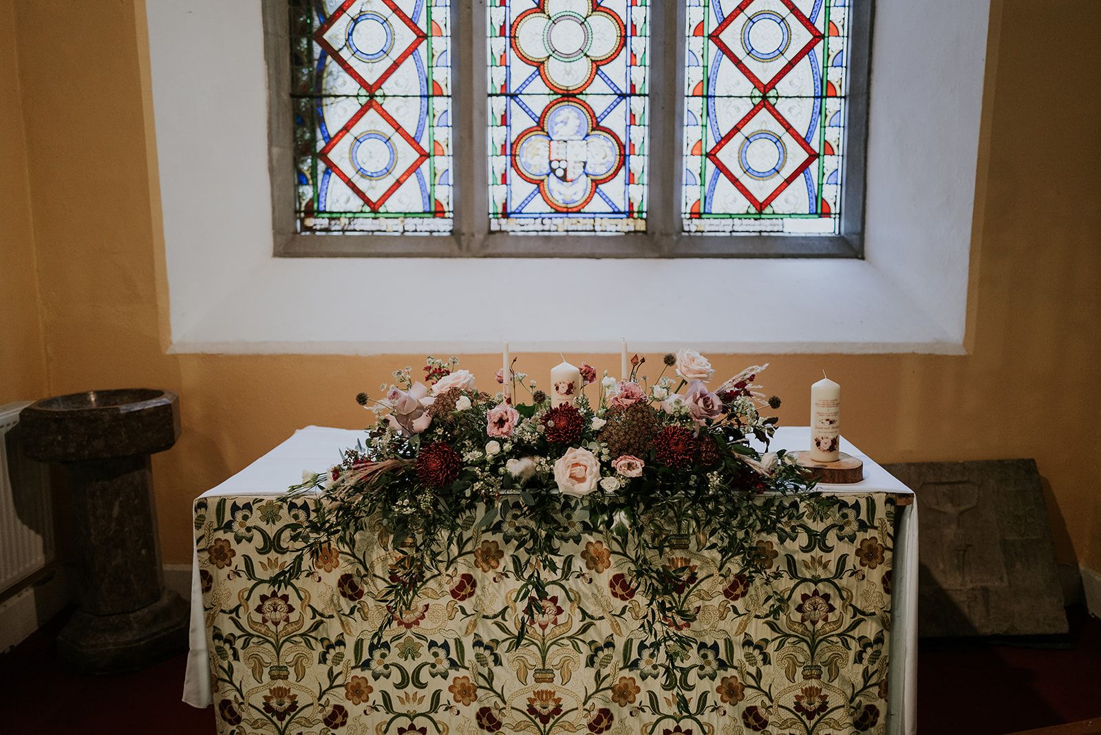 The altar at St. John's Church, Knockainey dressed for a wedding: burgundy and blush roses and candles under the red and blue stained-glass window.