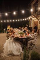 Bride and groom seated in a long table with their friends and family under string lights during their small wedding in Italy
