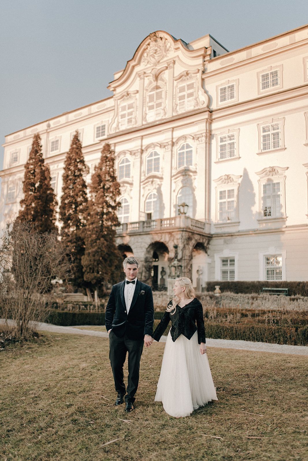 Bride and groom walking hand in hand in front of a baroque palace in Salzburg