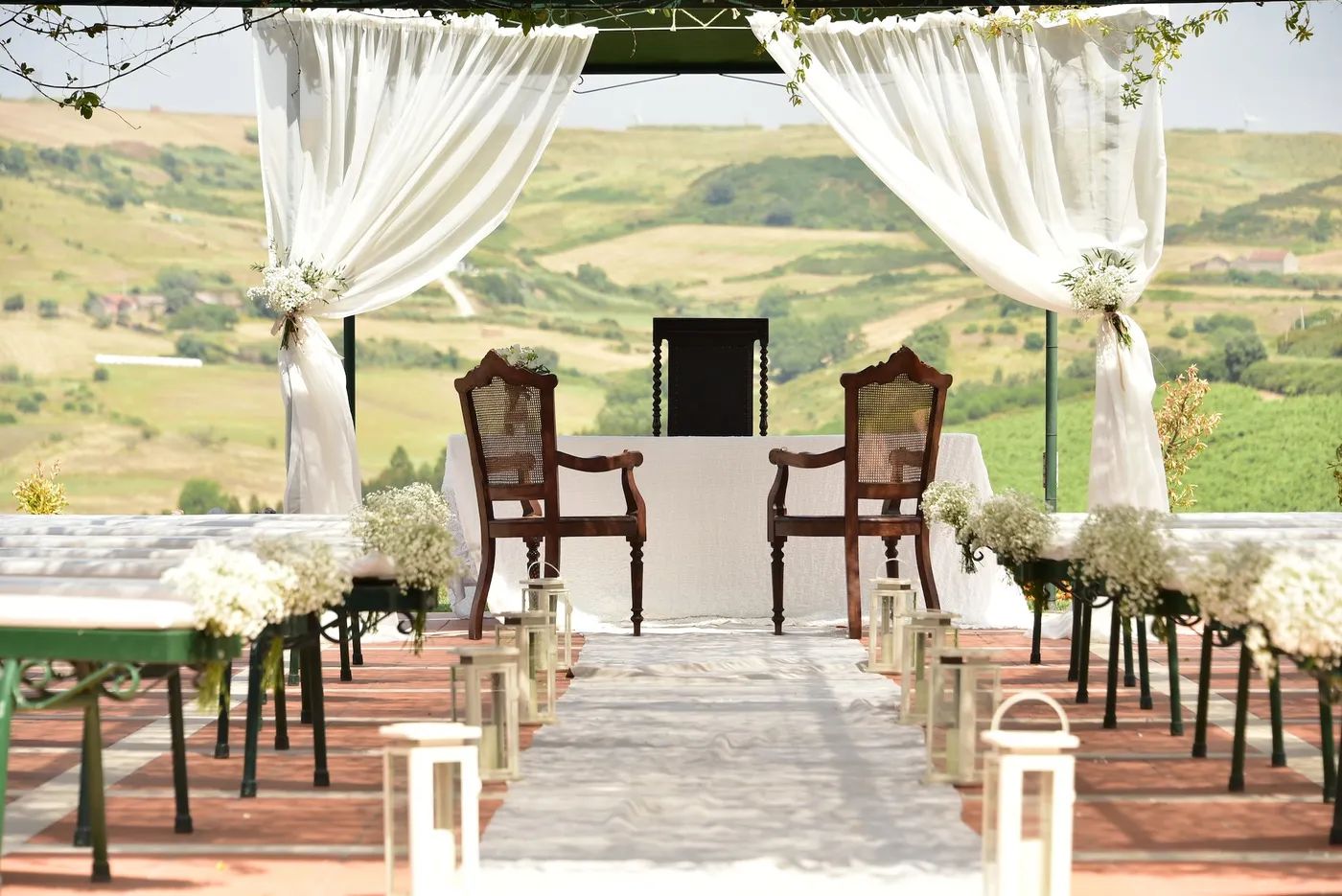 Two chairs facing a table with pews at the back, a cloth ceremony arch in front, and countryside views of Mafra in Portugal