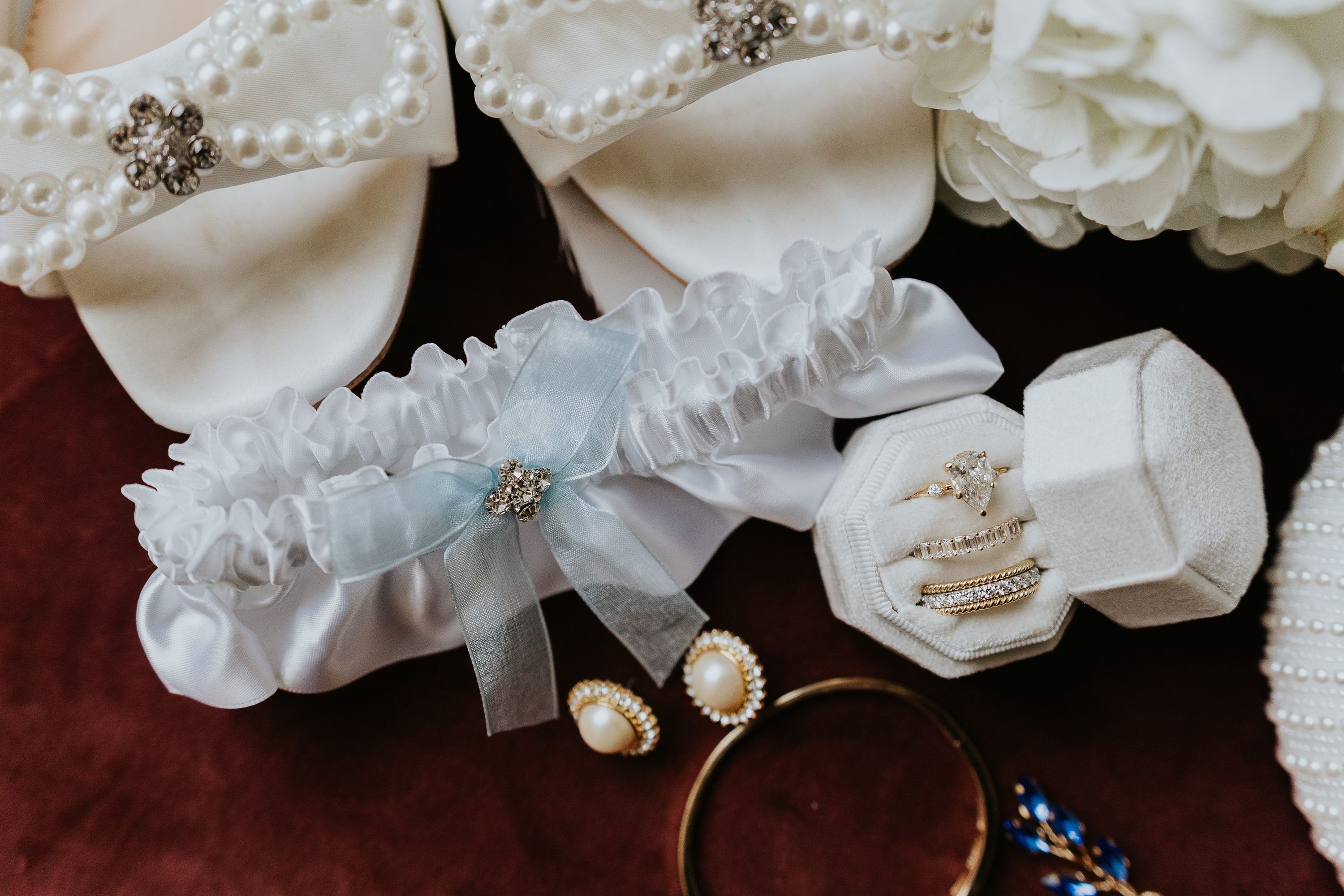 Wedding rings, garter, and bridal accessories prepared for an intimate wedding in Italy on a polished wooden table