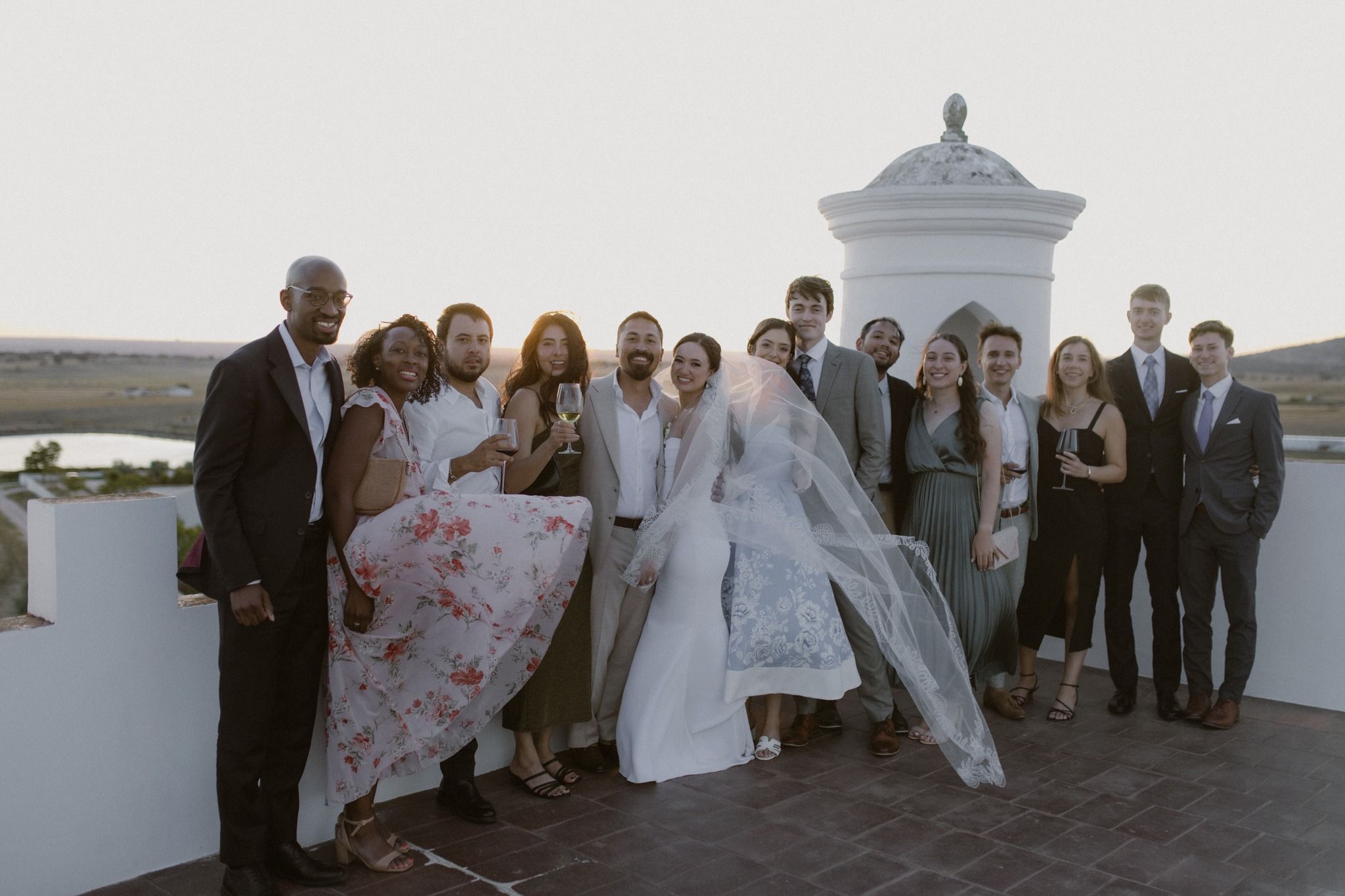 Bride and groom gather on the terrace with their guests during sunset for a wedding photoshoot