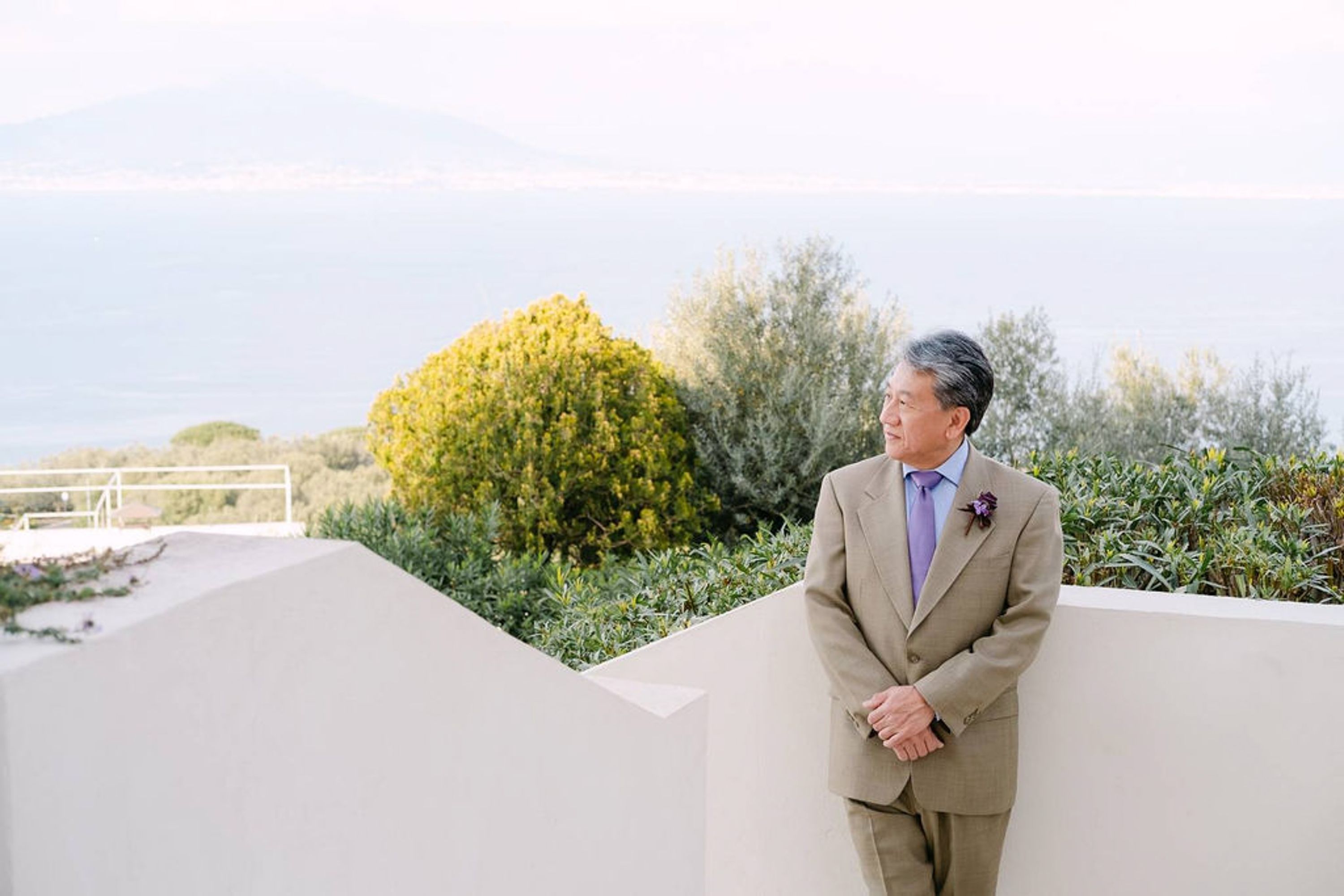 Groom standing on a terrace during a small wedding in Italy with panoramic coastal scenery behind him