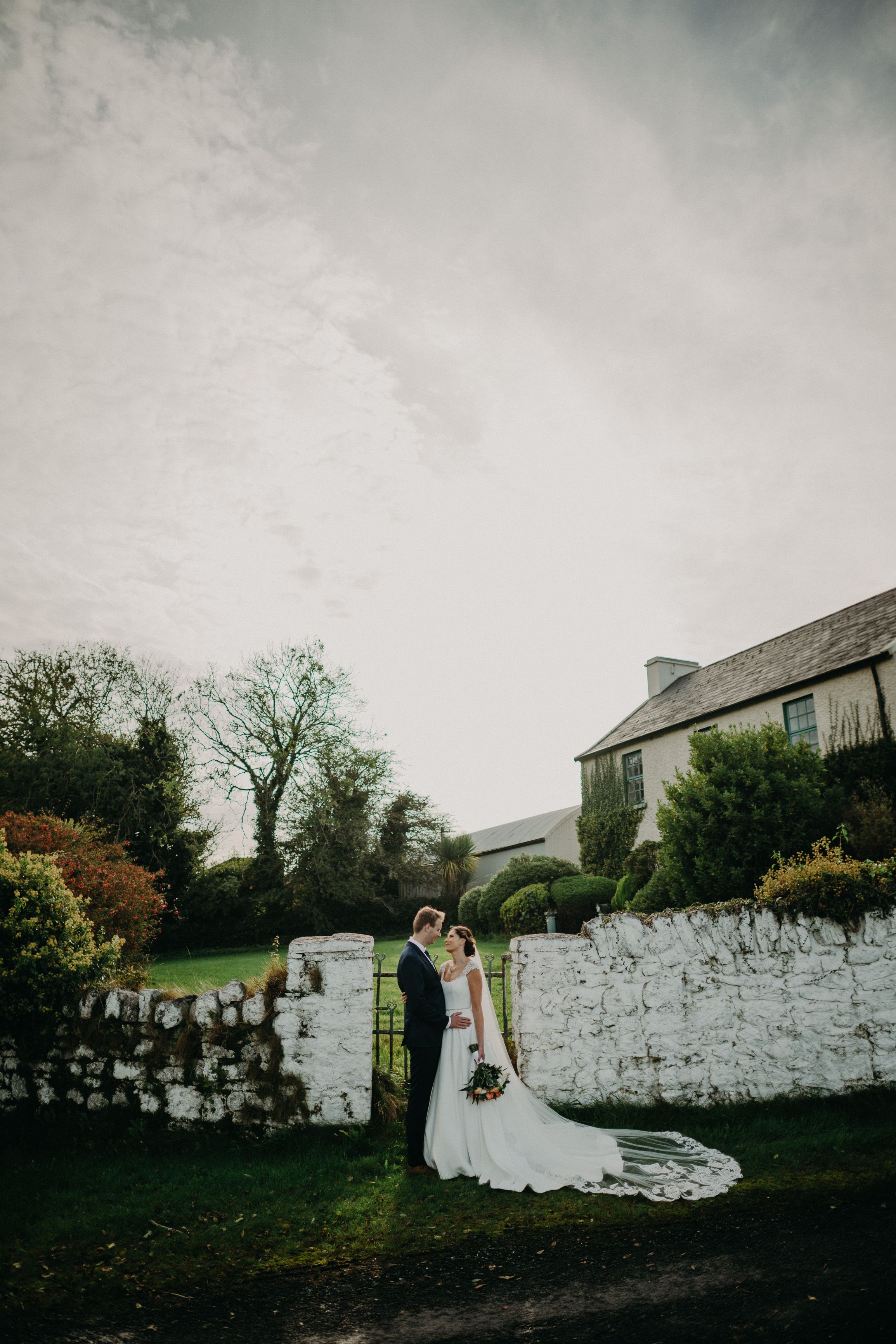 Intimate wedding in Ireland with bride and groom standing by a stone wall and gardens near a manor