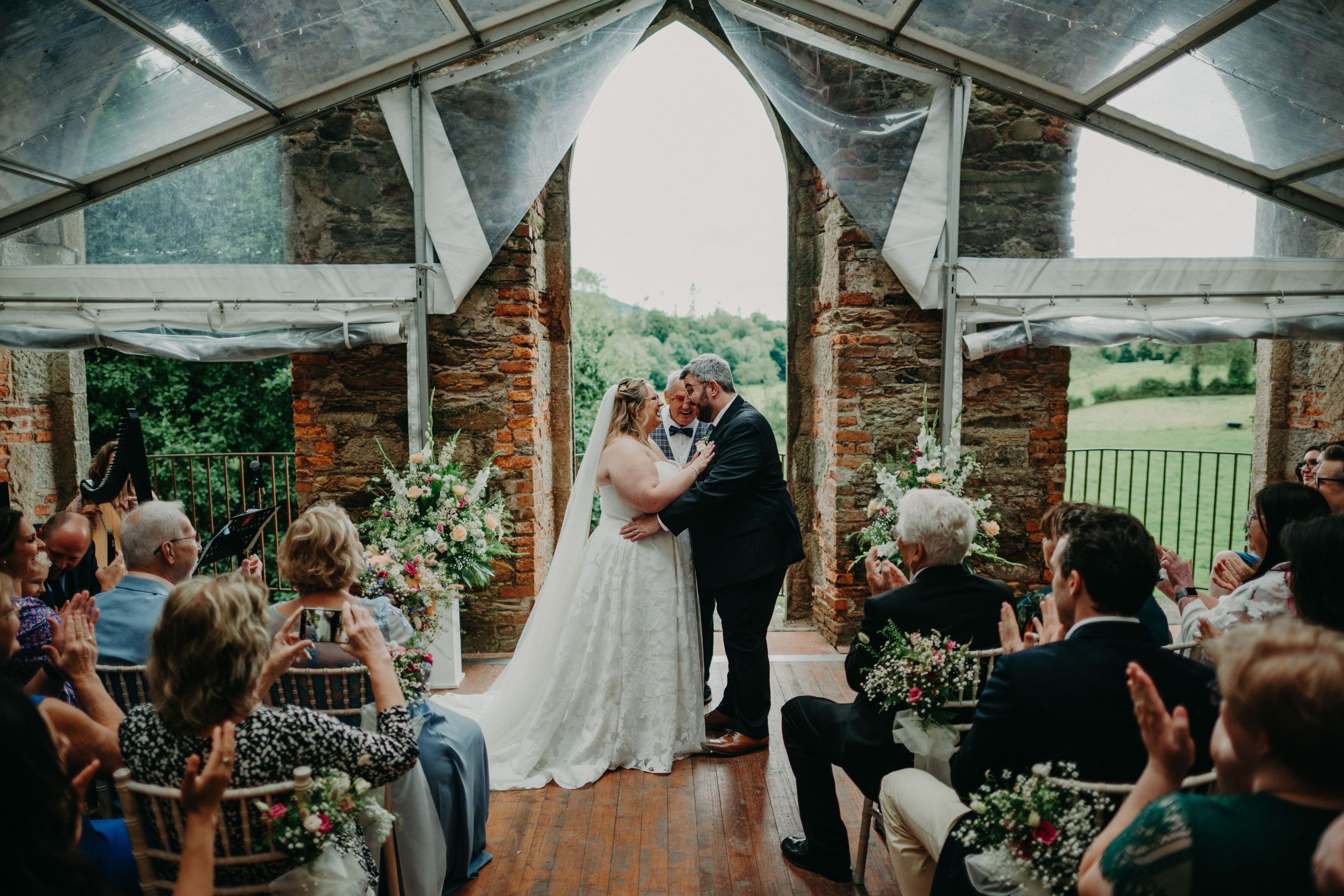 Bride and groom about to kiss in front of their guests inside a castle ruin with lush greenery in the background