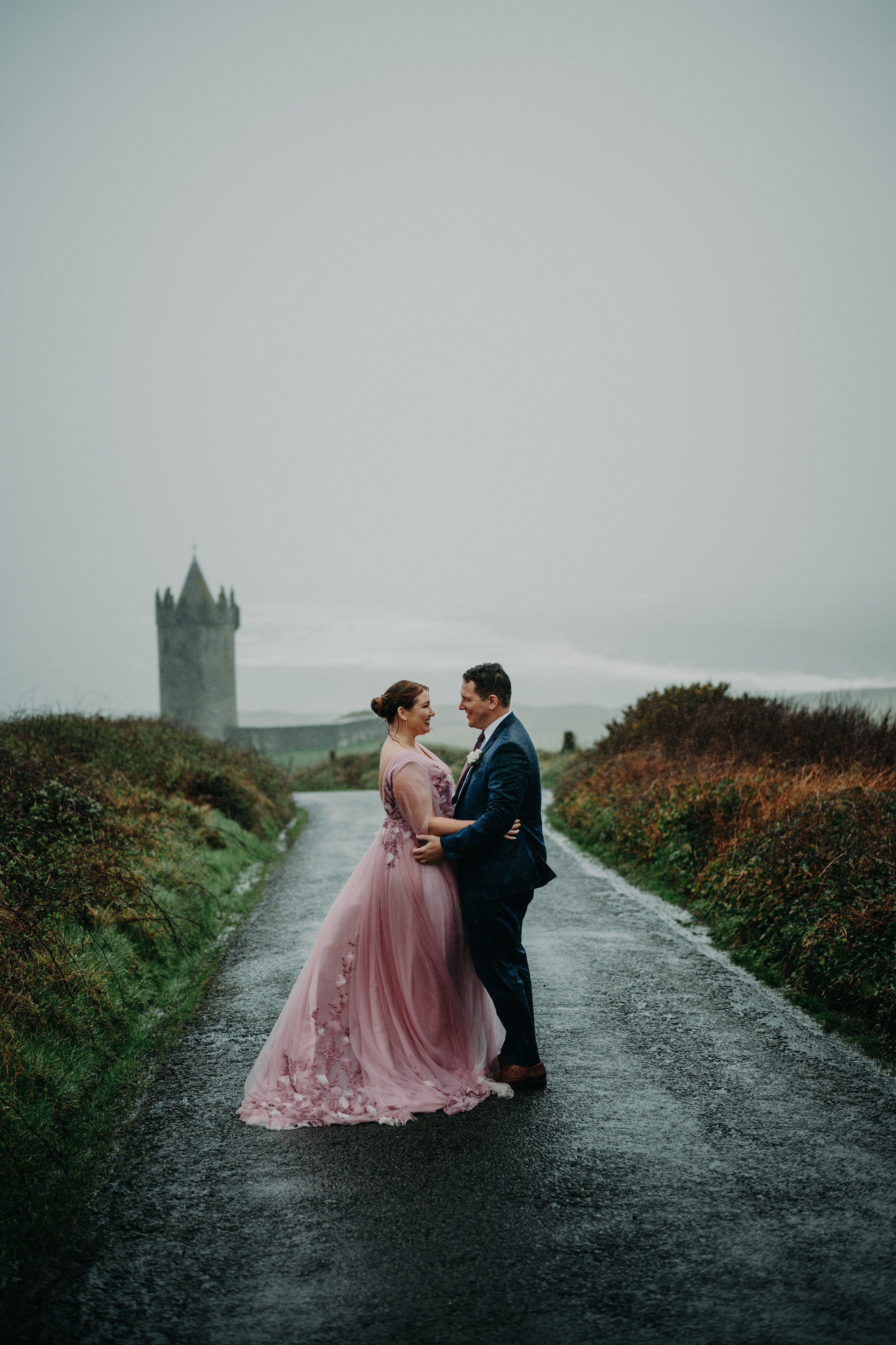 Bride wears pink dress hugging her groom in an outdoor spot while it’s drizzling during their elopement in Ireland