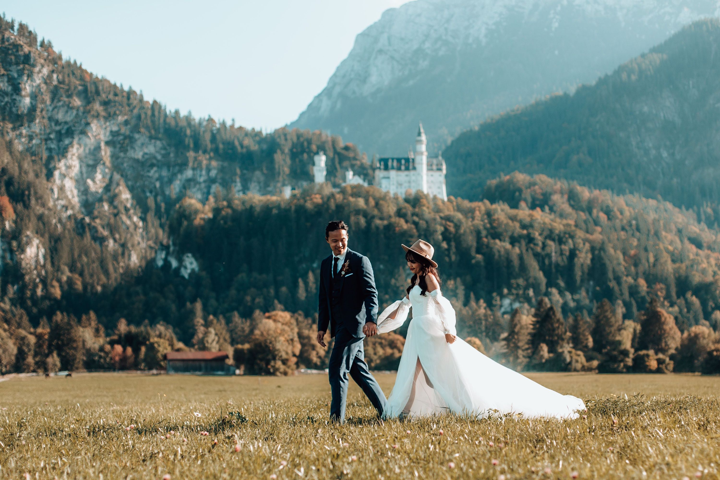 Eloping bride and groom walking in a field below Neuschwanstein castle in Germany