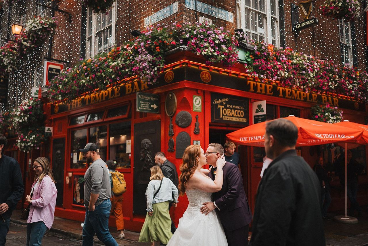 Newlyweds kissing in the middle of a crowd in Dublin during their elopement in Ireland with a quaint red building in the back