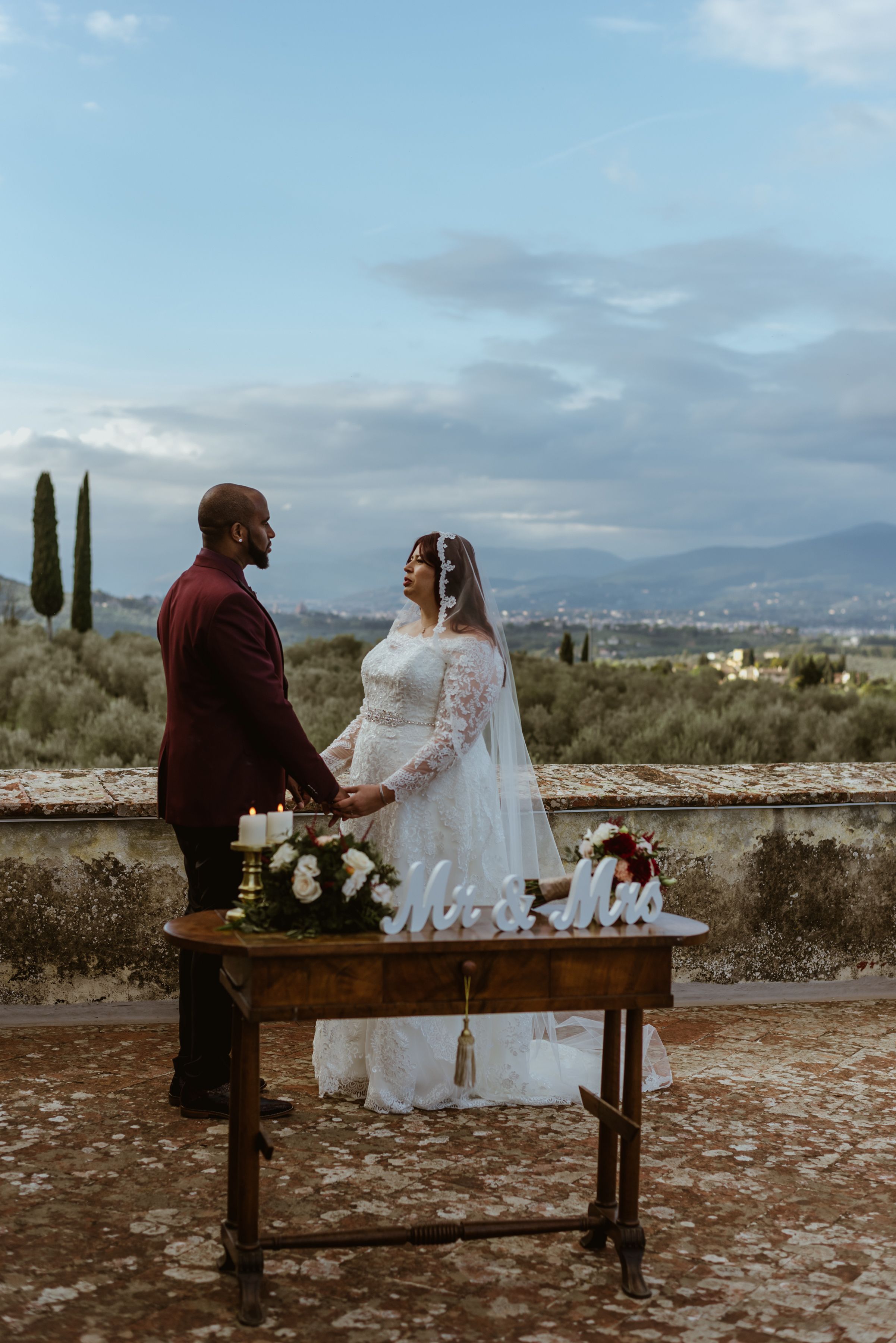 Bride and groom hold hands during their elopement ceremony in Tuscany on the terrace of the medieval villa where they got married