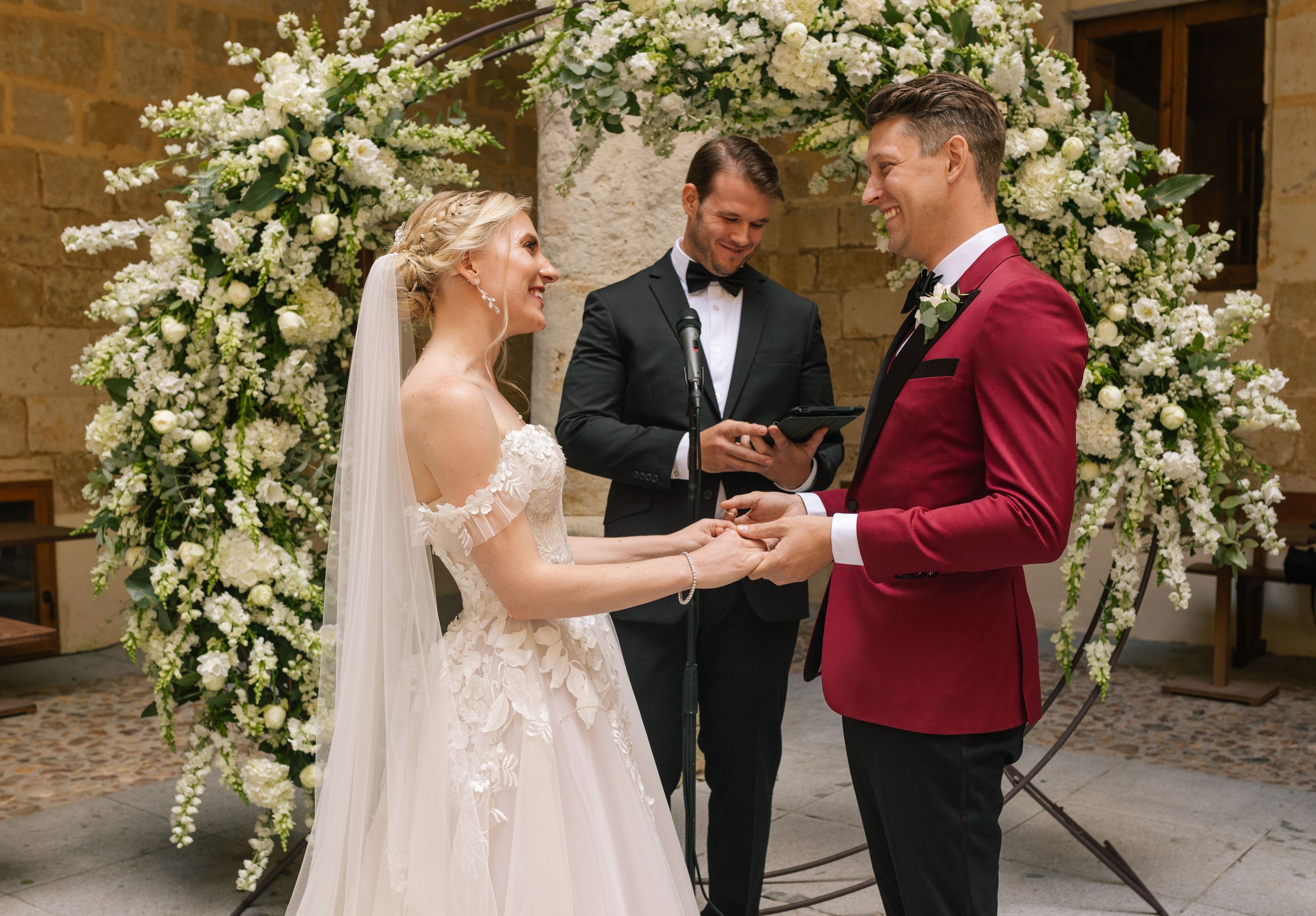 Bride and groom hold each other during the ceremony of their destination wedding in Spain, with a floral arch at the back