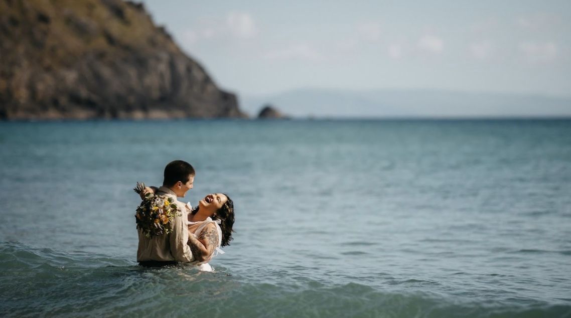Newlywed couple laughing and hugging half-submerged in an ocean in Ireland