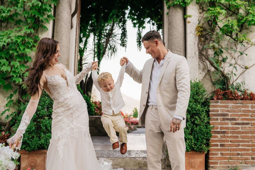 Bride and groom hold their little boy who jumps during the photoshoot of their micro wedding in Italy