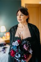 Bride wears a black wedding dress and a crown, and holds a purple and red bouquet for her Irish elopement