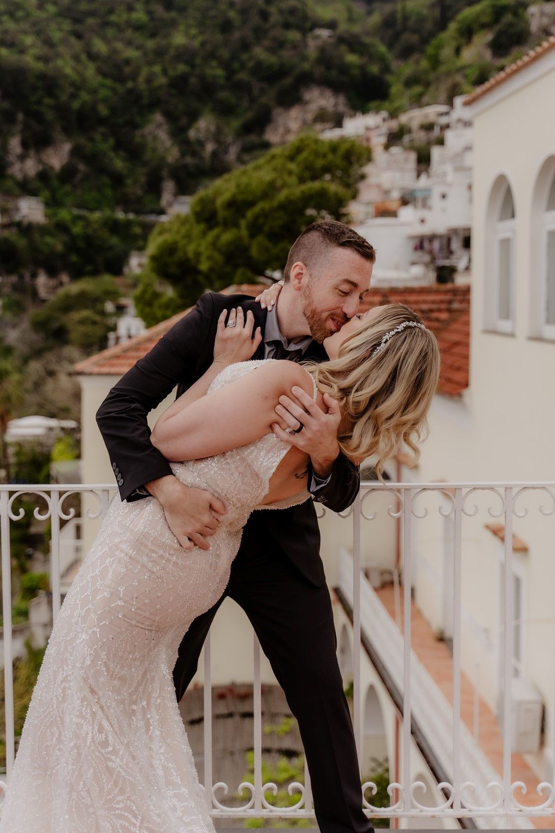 Groom kissing his bride on top of a terrace during their elopement in Italy with Amalfi coast views in the background