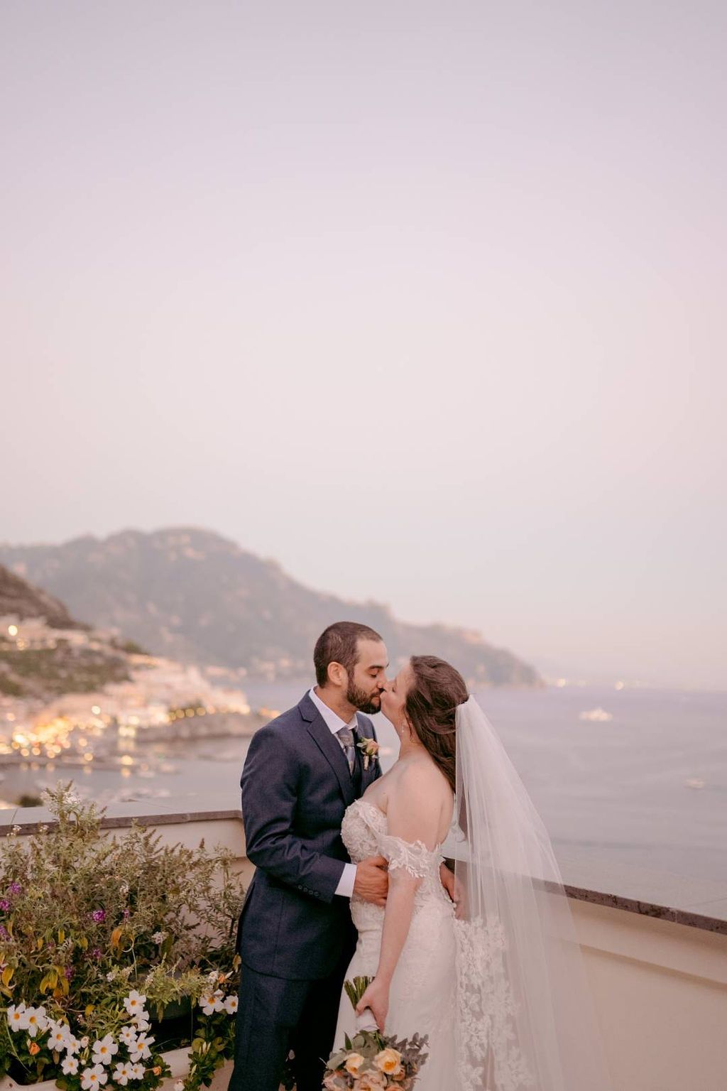 Bride and groom kissing during the photoshoot of their elopement in Italy, with the scenic Amalfi Coast in the background