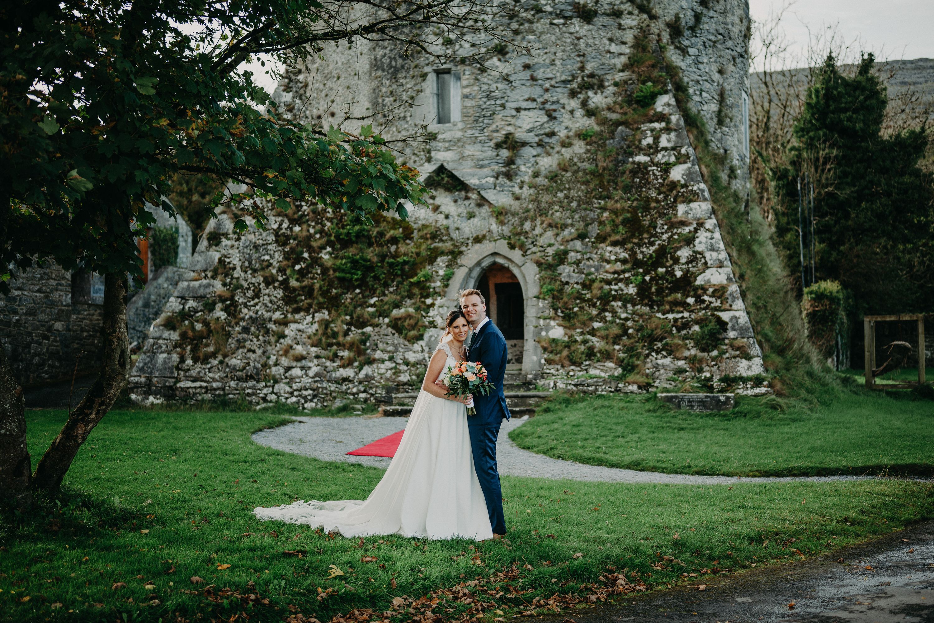 Bride and groom pose outside a historic castle tower during an intimate wedding in Ireland surrounded by lush countryside.