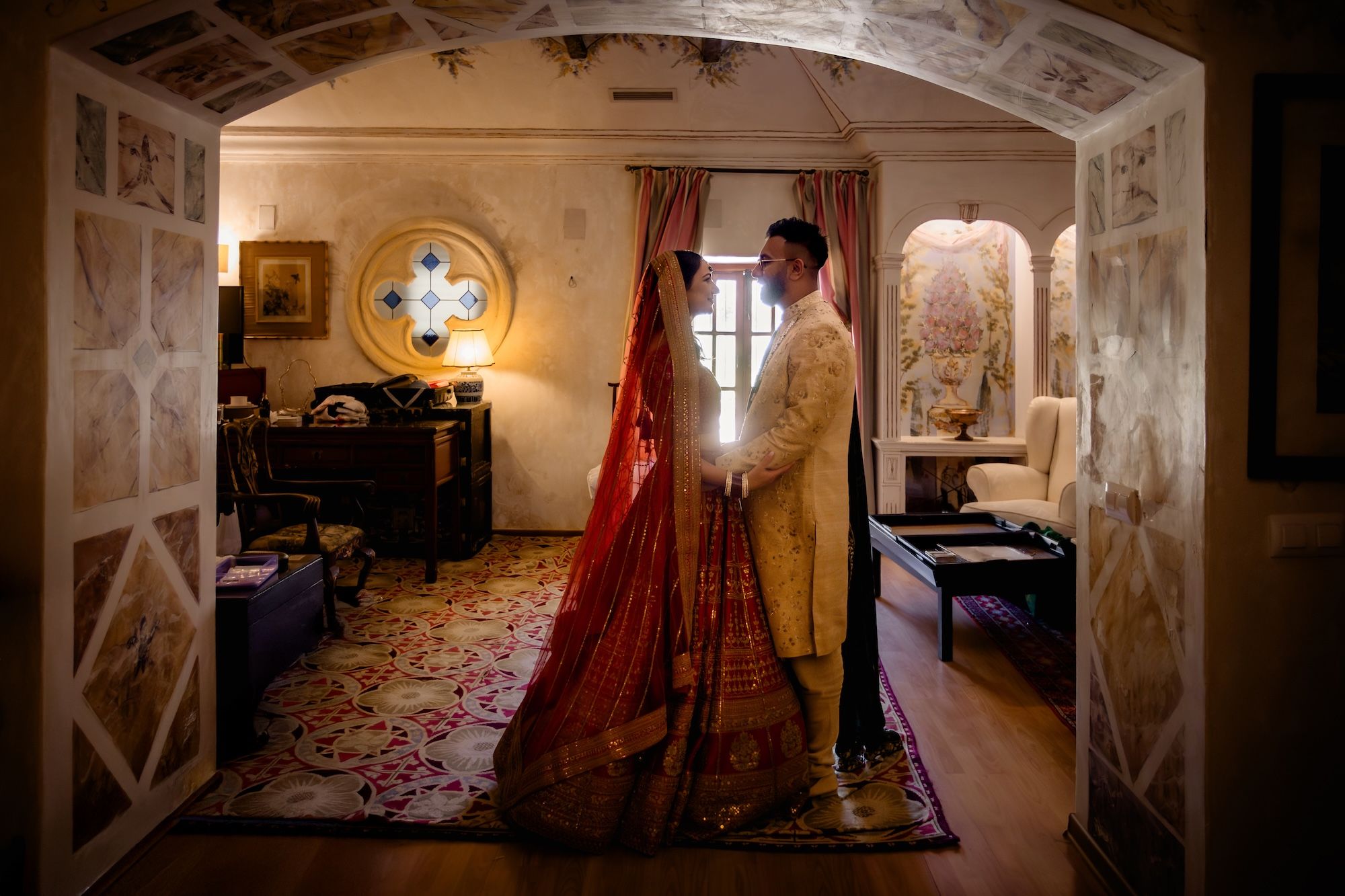 Bride and groom wearing traditional Hindu attire looking at each other inside a room for their destination wedding in Spain