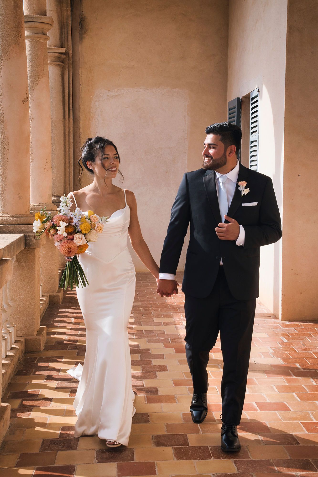 Bride and groom holding hands while the bride holds her spring themed bouquet during their destination wedding in Spain