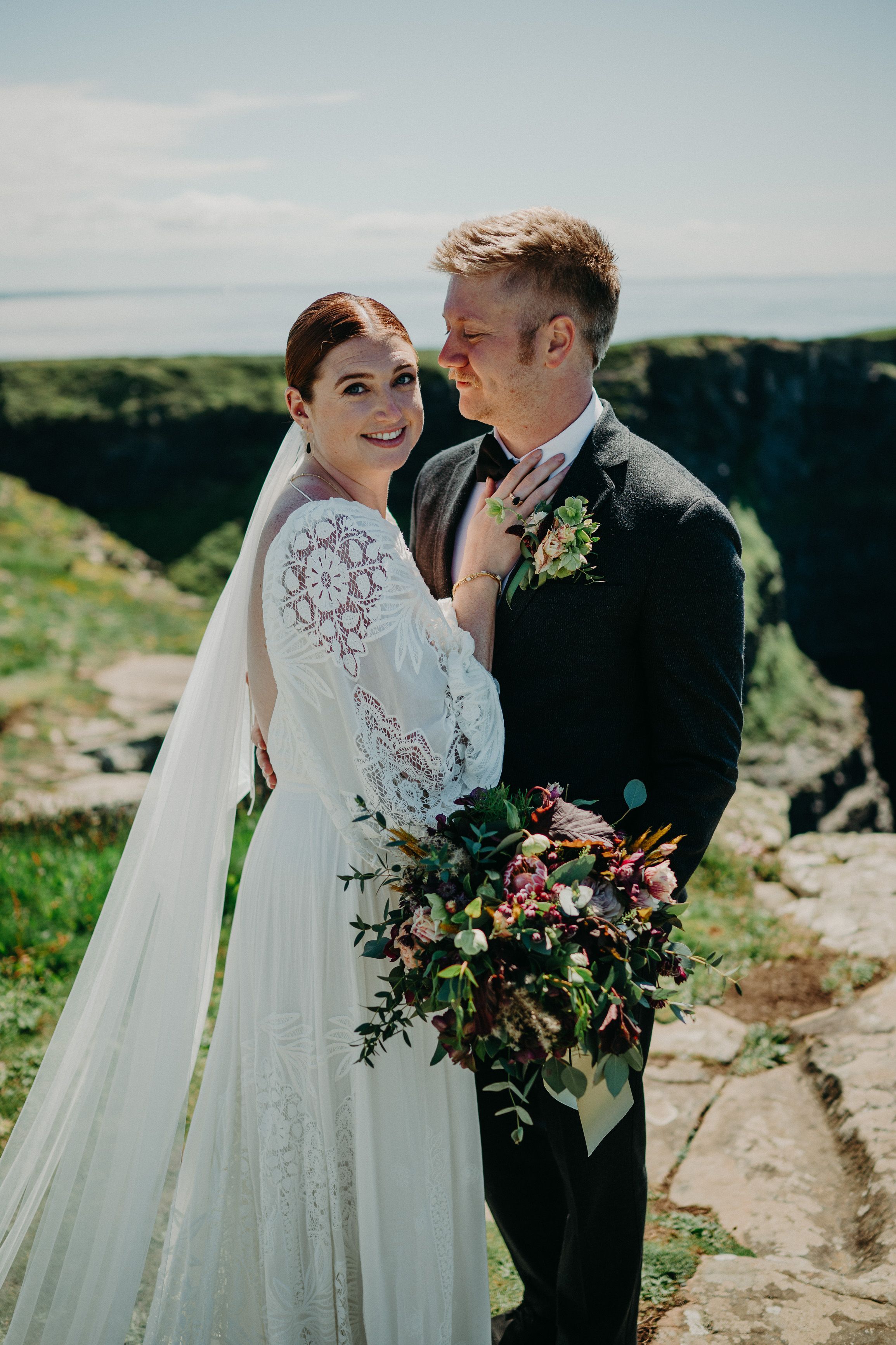 A bride and groom standing on a beautiful cliff with an amazing ocean view after their intimate wedding in Ireland