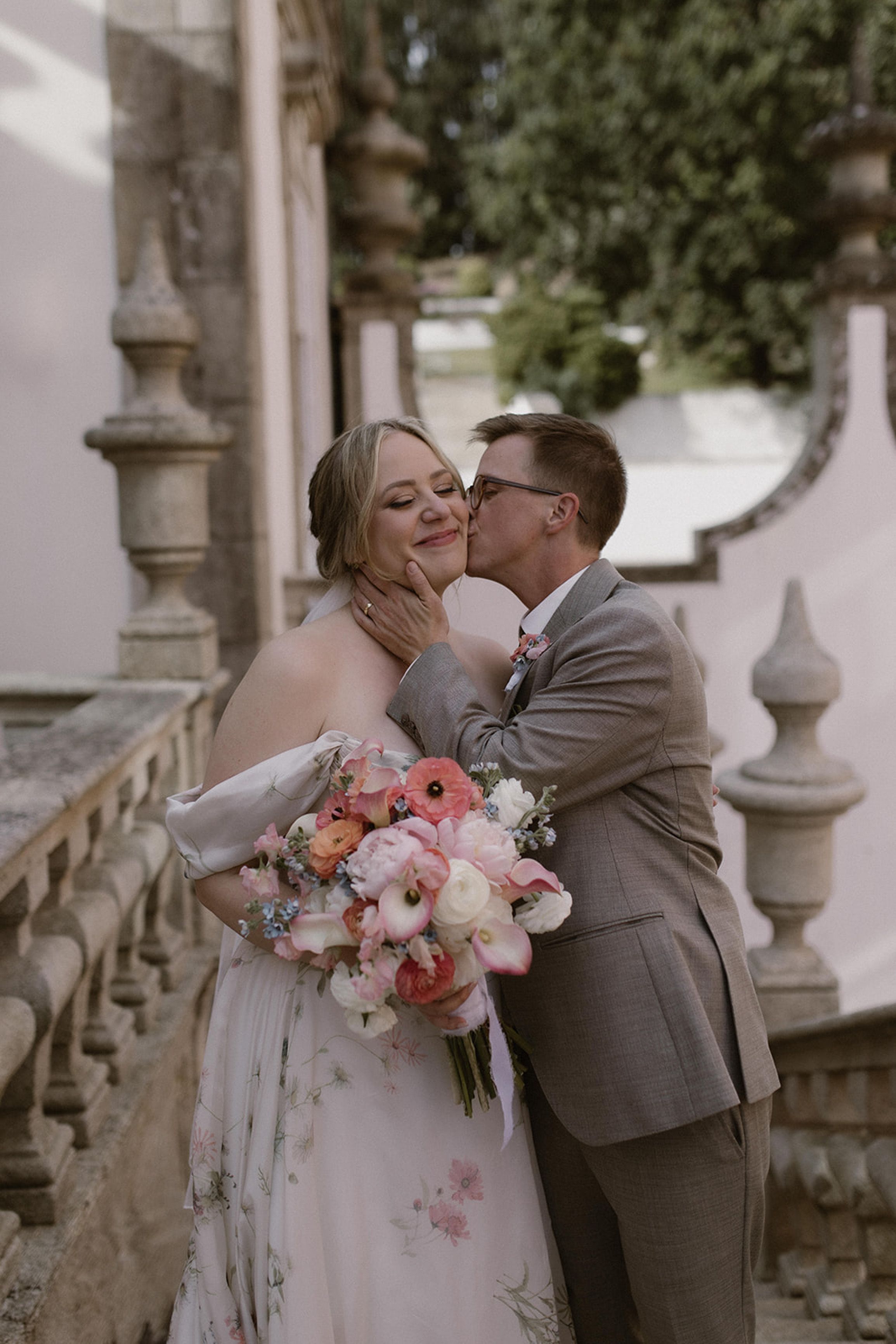 Groom kissing the bride's cheek while she holds a pastel bouquet at an intimate wedding in Portugal