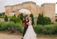 Bride and groom posting with an umbrella in front of a historic castle in Spain