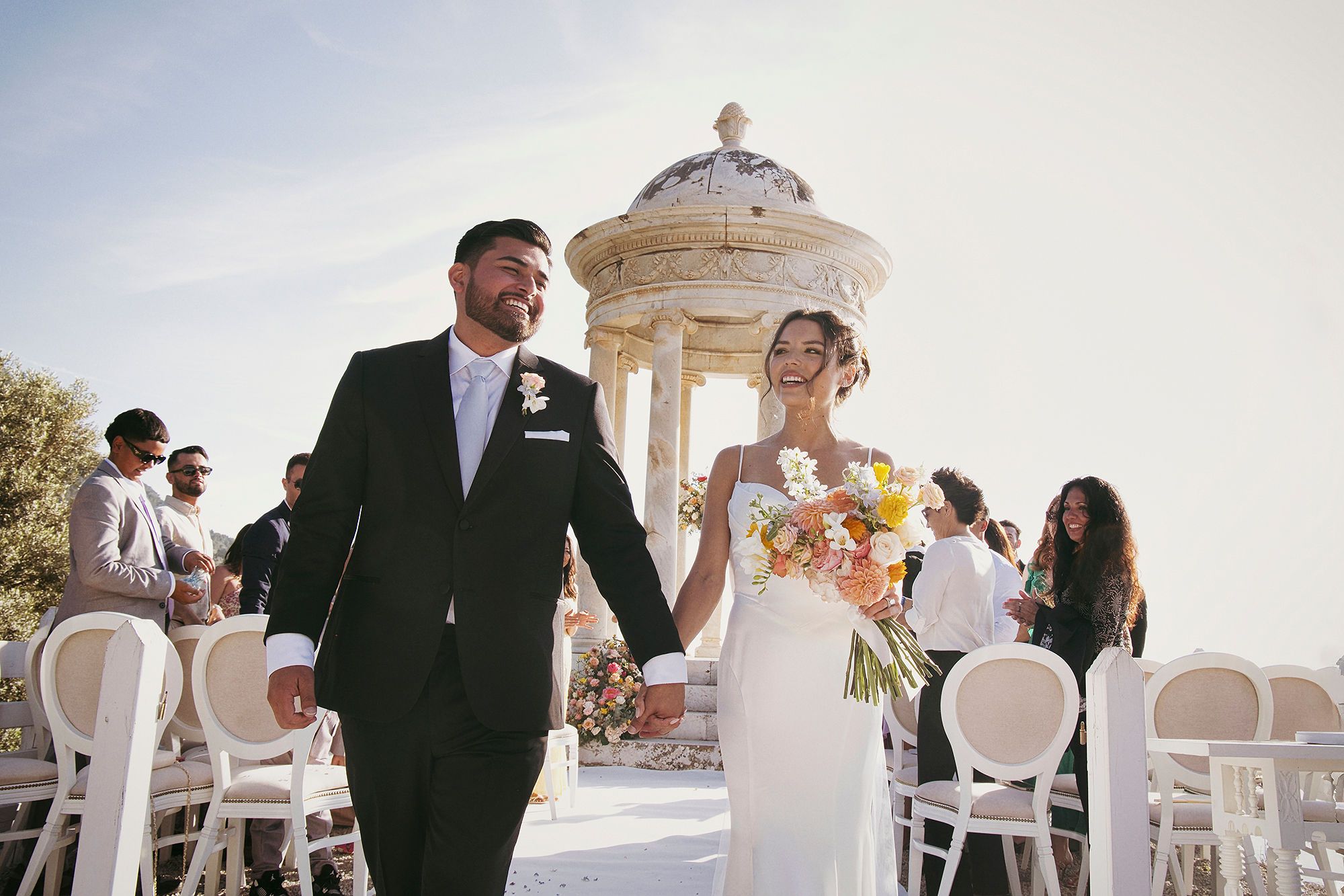 Newlyweds happily walking down the aisle while holding hands in an outdoor setting of their ceremony in Mallorca, Spain
